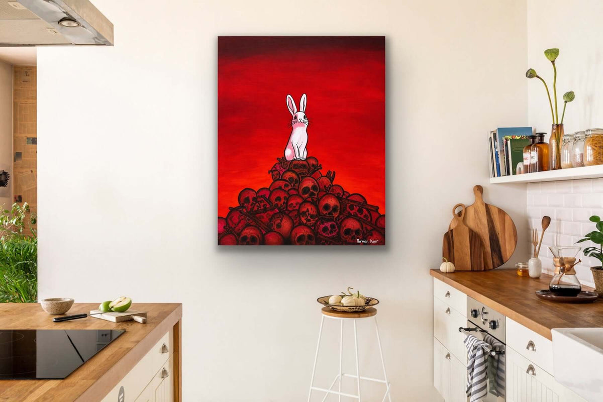 The Rabbit Among Skulls Art Print displayed in a kitchen, featuring a white rabbit atop a pile of skulls with a dramatic red background.